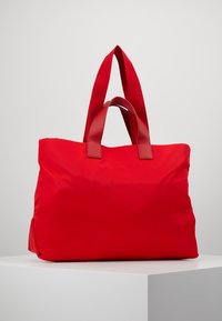 Bolsa de mano de nailon rojo con una textura suave, que presenta dos asas superiores de cuero rojo, una apertura amplia y sin hardware ni adornos visibles.