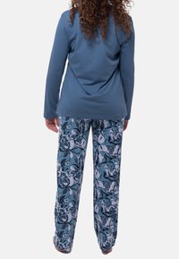 Maglia a maniche lunghe blu abbinata a pantaloni da pigiama con motivo floreale. I pantaloni presentano grandi fiori bianchi e blu scuro su uno sfondo blu chiaro.