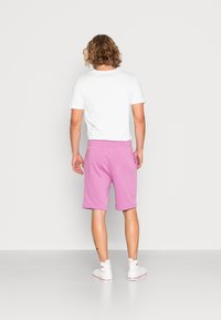 Camiseta blanca de manga corta combinada con pantalones cortos de algodón rosa. Los pantalones cortos tienen una longitud hasta la rodilla, con un corte holgado y una cinturilla elástica.