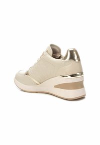 Le scarpe da ginnastica beige presentano una parte superiore testurizzata, un accento metallico sul tallone, una suola imbottita e un design a zeppa. Inclusi lacci e dettagli di cucitura.