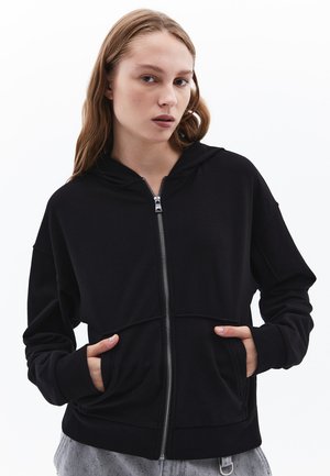 Felpa nera con zip realizzata in tessuto morbido, dotata di cappuccio, tasche frontali e polsini a costine. Design semplice con una vestibilità comoda.
