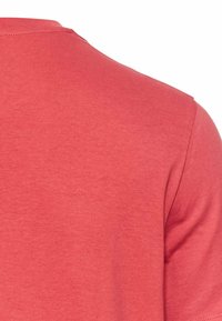 Kortærmet t-shirt i lys koral, lavet af blød, glat bomuld. Rund halsudskæring og rene sømme, med en subtil tekstur.