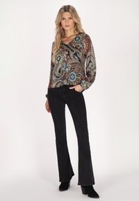 Jeans neri a zampa d'elefante abbinati a una blusa a maniche lunghe con scollo a V che presenta un vivace motivo paisley nei toni del blu, arancione e crema.
