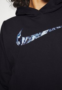 Personne portant un sweat à capuche noir avec un grand logo Nike Swoosh bleu et blanc réfléchissant sur la poitrine.