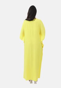 Robe longue jaune avec une silhouette ample et fluide, manches courtes et un tissu texturé. Présente des poches latérales pour un usage pratique.