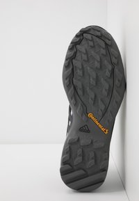 Suela de zapato deportivo negro con un patrón de dibujo robusto. Presenta los logotipos "Continental" y "adidas" en acentos naranjas y negros. Superficie texturizada.