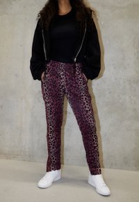 Pantaloni con stampa leopardata in tonalit à di viola e nero, dotati di vita con cordoncino, tasche laterali e abbinati a sneakers bianche. Giacca nera con zip.
