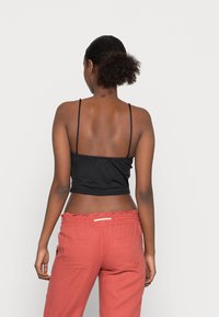 Top cropped preto com alças finas, combinado com calças largas cor de coral, com uma cintura elástica e bolsos traseiros.