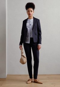 Černý tailored blejzr, bílá blůza, přiléhavé černé kalhoty, béžová taška a tělové baleríny. Hladká látka, strukturovaný design, minimální detaily.