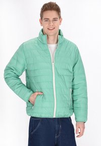 Giacca piumino leggera verde menta con colletto alto, chiusura con zip, tasche laterali e sottili particolari di cucitura orizzontale.