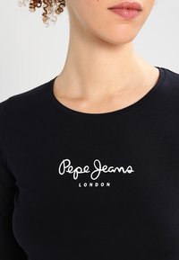 Schwarzes, eng anliegendes T-Shirt aus Baumwolle, mit rundem Halsausschnitt und weißem "Pepe Jeans London"-Logo auf der Vorderseite. Glatte Textur.