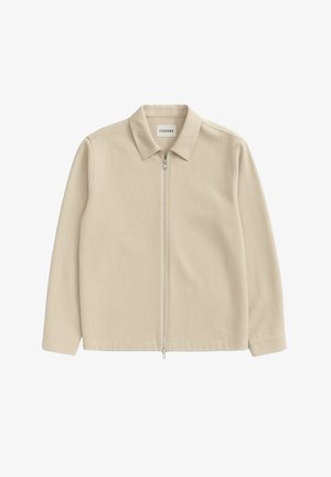 Beige Zip-Jacke mit Kragen, langen Ärmeln, glatter Textur und minimaler Ausstattung; das Etikett trägt die Aufschrift "CISZERE."