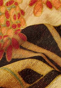 Textile avec un motif doré et noir, comprenant des motifs floraux en rouge et vert. Matériau doux et texturé avec un éclat métallique.