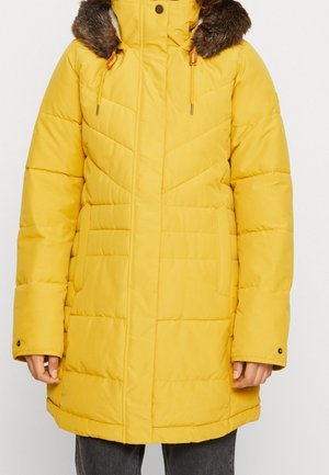 Gelbe, gesteppte Winterjacke mit einem mit Fell besetzten Kapuzen, Fronttaschen und Zugbändern, getragen über dunklen Hosen.