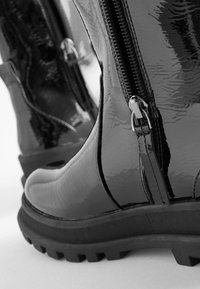 Schwarz glänzende Knöchelstiefel mit strukturiertem Finish, ausgestattet mit zwei seitlichen Reißverschlüssen und robusten Sohlen, die ein stabiles Design für den ganztägigen Gebrauch bieten.