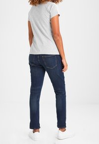 Šedá polokošile s krátkým rukávem v kombinaci s tmavě modrými slim džíny. Oblečení doplňují bílé tenisky, což vytváří ležérní vzhled.