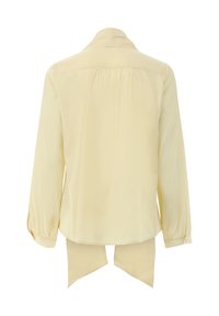 Gelbe Bluse mit langen Ärmeln, hohem Kragen, Rückenfalten und Bindebändern am Saum. Hergestellt aus leichtem Stoff mit glatter Textur.