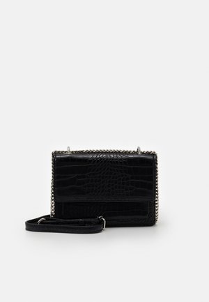 Sort crossbody taske i krokodilleskind med sølvkæde som rem og rektangulært klaplukning på hvid baggrund.