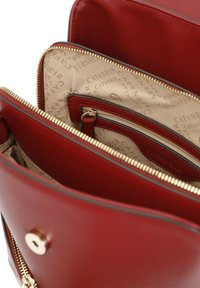 Borsa a mano in pelle rossa con zip e accessori in oro, dotata di un interno beige con motivo, molteplici tasche e chiusura a scatto.
