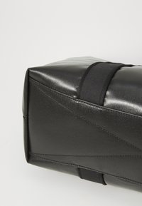 Bolsa retangular preta com uma superfície texturizada, apresentando alças de tecido pretas e costuras angulares, destacando um design moderno.