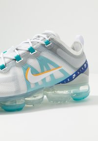 Chaussure Nike Air VaporMax blanche et grise avec des accents turquoise et orange et une semelle à coussin d'air transparente teintée de bleu.