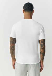 White short-sleeve jersey t-shirt with ribbed texture, crew neck, and a fitted design, worn with light gray sweatpants.