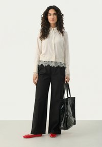 Cream long-sleeve blouse with lace hem, black wide-leg trousers, red flats, and a glossy black tote bag.