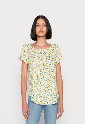 Blusa floral de manga curta com um fundo verde claro, flores amarelas e brancas, decote redondo e um polozinho ligeiramente curvado.