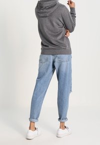 Grå huvtröja med mjuk textur, bärs med ljusblå löst sittande jeans och vita sneakers med svarta snören.