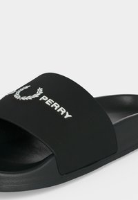 Sandale noire slip-on avec semelle surélevée, texte brodé "PERRY" blanc et logo de laurier sur la large sangle.
