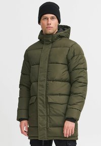 Maslinasto zelena jakna s punjenjem s visokim ovratnikom, prednjim zatvaračem i dva aplikirana džepa. Ima kapuljaču i kviltanu teksturu.