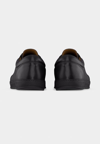 Ζευγάρι μαύρα δερμάτινα αθλητικά παπούτσια, ορατά από πίσω, που δείχνουν ομαλή υφή και ελαφρώς ανυψωμένες φτέρνες πάνω σε απλό λευκό φόντο.