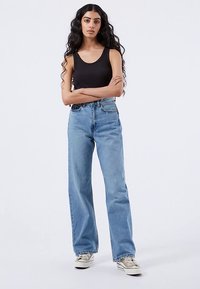 Džíny s vysokým pasem, širokými nohavicemi, světle modré barvy s vybledlým efektem, bočními kapsami a kontrastním prošitím, doplněné černým tílkem.