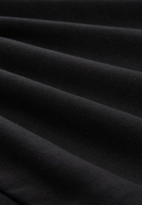 Tela negra con una textura suave, que presenta pliegues que crean profundidades y sombras variadas, reflejando una luz suave sobre la superficie.