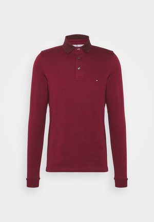 Langärmeliges burgunderfarbenes Poloshirt mit drei Knöpfen und kleinem Logo auf der linken Brust, vor einfarbigem Hintergrund präsentiert.