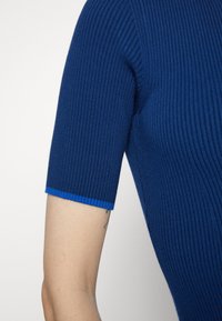 Niebieski prążkowany top z krótkimi rękawami. Manżety rękawów ozdobione kontrastową niebieską lamówką. Miękka faktura i dopasowany krój są widoczne.