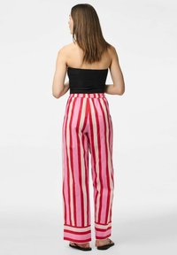Pantalons rayés en rouge et rose avec une coupe large et une taille élastique. Le matériau semble léger avec une texture lisse.