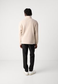Beige fleece pullover with high collar, relaxed fit and ribbed cuffs, paired with black pants and white sneakers. Minimalist design.
