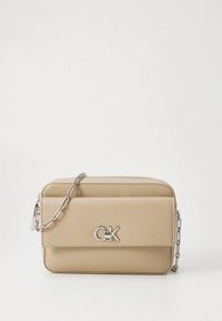 Bež pravokotna usnjena torbica čez ramo s srebrnim verižnim trakom in srebrnim CK logotipom na zaponki sprednjega žepa.