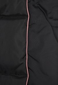 Svart vadderat jacktyg med quiltade sektioner. Har ljusrosa kantband längs sömmarna. Slät textur med en svag glans.