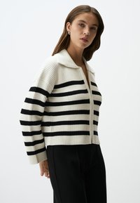 Cardigan a righe bianco e nero, con colletto, texture a coste, zip frontale e lunghezza cropped. Abbinali a pantaloni neri.