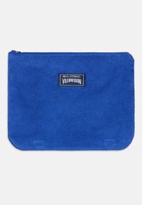 Bolsa de tela azul con textura suave, esquinas redondeadas y una etiqueta con logotipo negro. Cremallera cerrada en la parte superior para un almacenamiento seguro.