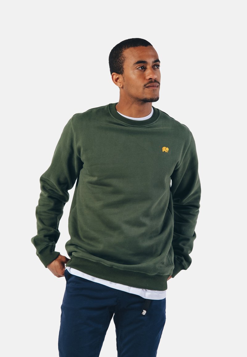 Grøn sweatshirt med et struktureret stof, rund halsudskæring, ribbede manchetter og et lille gult elefantlogo på brystet. Bæret over en hvid t-shirt.