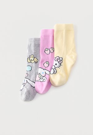 Kolm värvikat laste sokki hallis, roosas ja kollases, millel on mängulised multifilmitegelased ja puuvilja motiivid, laotatud valgele taustale.