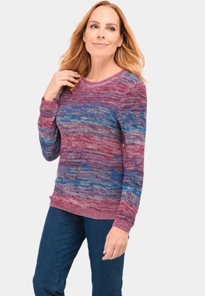 Strickpullover mit einem mehrfarbigen Muster aus lila, rosa und blauen Farbtönen, runder Ausschnitt und gerippten Bündchen. Kombiniert mit dunklen Jeans.