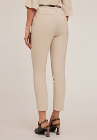 Pantaloni beige su misura con un taglio slim, caratterizzati da una texture liscia, tasche posteriori e una cintura elegante. Abbinati a scarpe con tacco dalla texture.