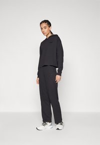 Felpa nera cropped con maniche lunghe e logo ricamato, abbinata a pantaloni della tuta neri con tasche laterali. Scarpe da ginnastica bianche.