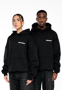 Felpe nere con cappuccio e tasca frontale, con la scritta "MULTIPLY" in bianco sul petto. Realizzate in tessuto morbido, con una vestibilità ampia e cappuccio regolabile.