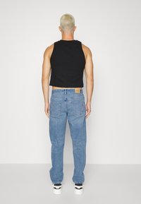 Černý žebrovaný zkrácený top, který je kombinován se světle modrými rovnými džíny s zadními kapsami a viditelným nápisem značky.