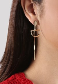 Goldfarbene Tropfohrringe mit einem trauerförmigen oberen Teil, einer halbkreisförmigen Form und einem hängenden zylindrischen Element mit strukturiertem Finish.